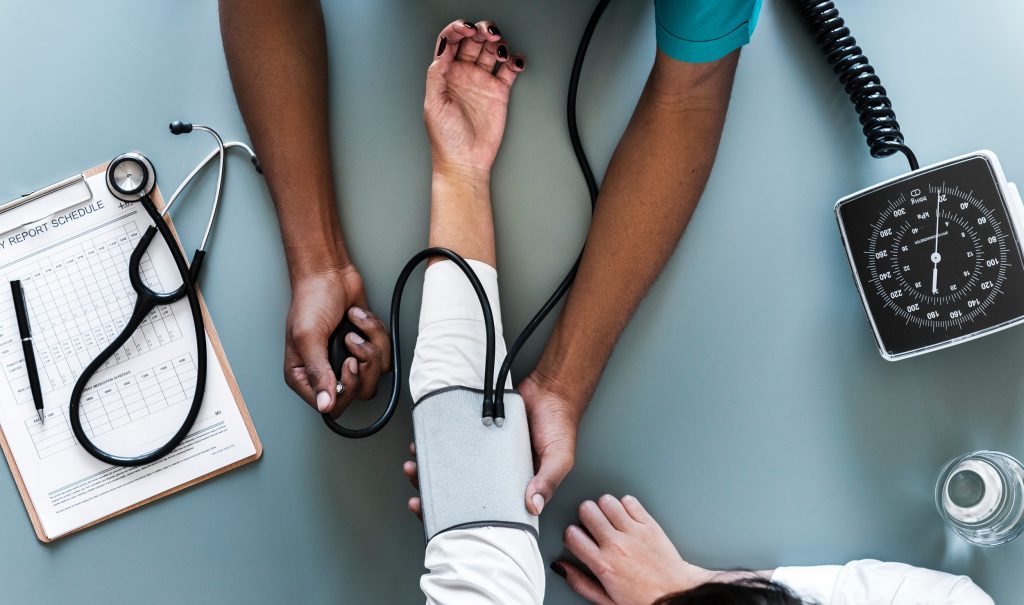 Ein Schwarzer Arzt, der an einem weißen Patienten den Blutdruck misst.