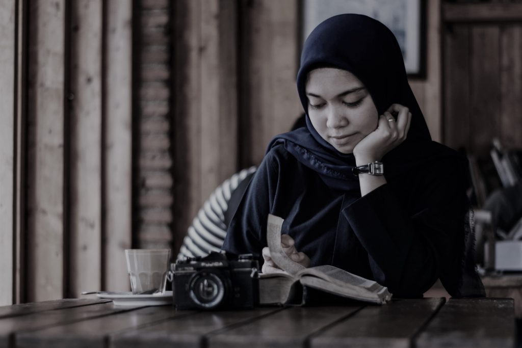 Frau mit Hijab liest in einem Cafe.