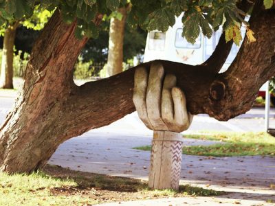 Baum der durch große geschnitzte Hand aus Holz abgestützt wird